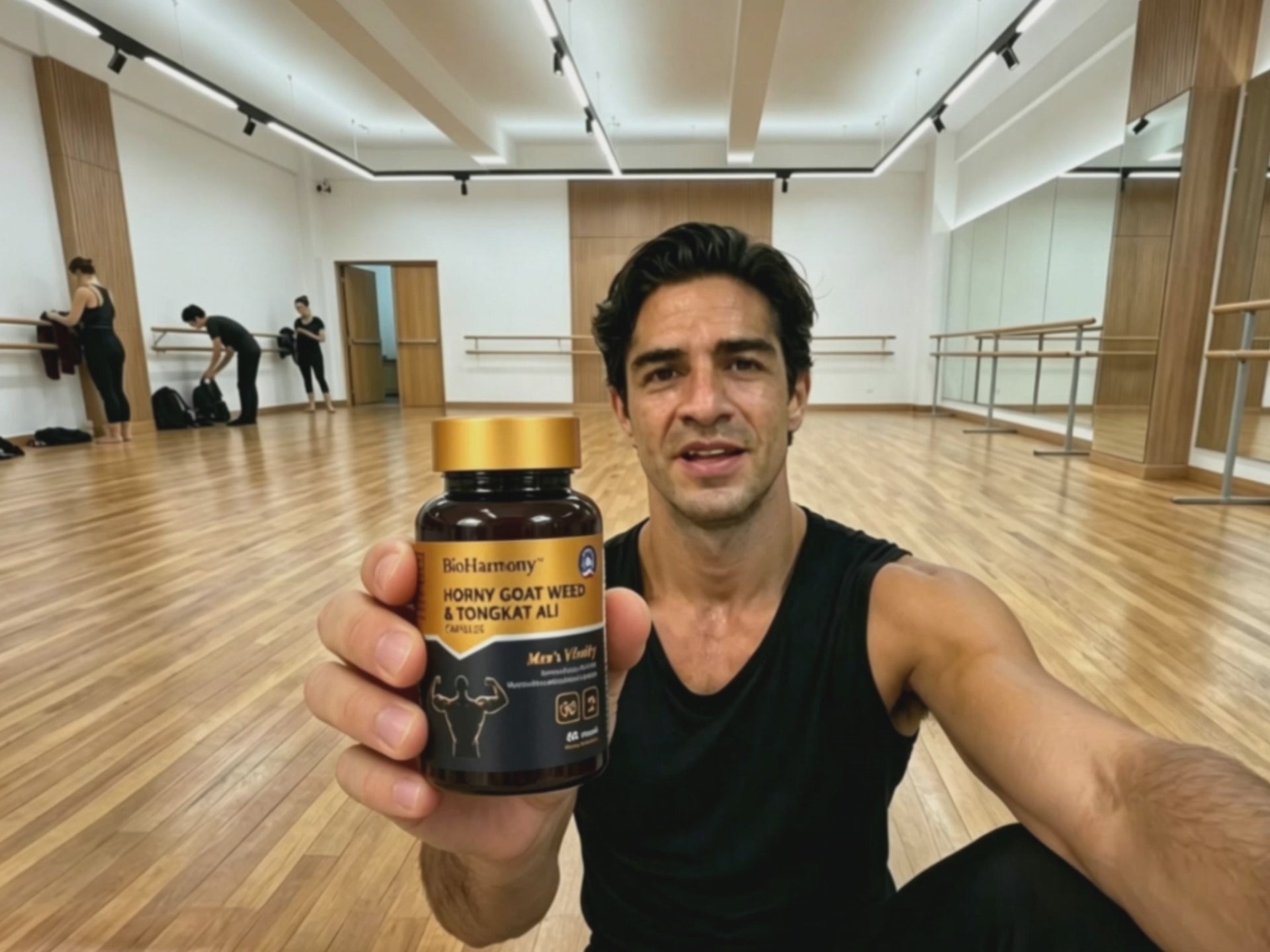 A man in a dance studio holding a BioHarmony Horny Goat Weed & Tongkat Ali bottle toward the camera. (影片 / video)