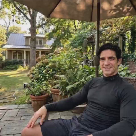 A man relaxing in a sunny backyard under an umbrella, smiling while holding up a BioHarmony Oyster Peptide & Maca bottle. (影片 / video)